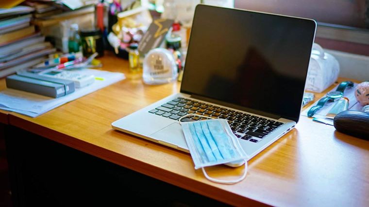 Photo of a busy desk, with a laptop and a mask