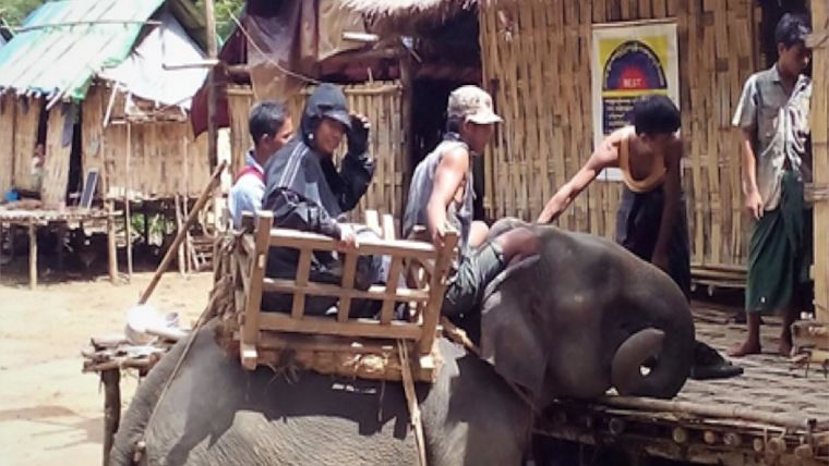 Three men on an elephant in a village in rural Myanmar