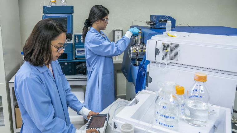 Two scientist, Dr Phornpimon Tipthara Wong and Senior Analyst Siribha Apinan wearing lab coats and operating the high-resolution Triple-TOF LC-MS system.